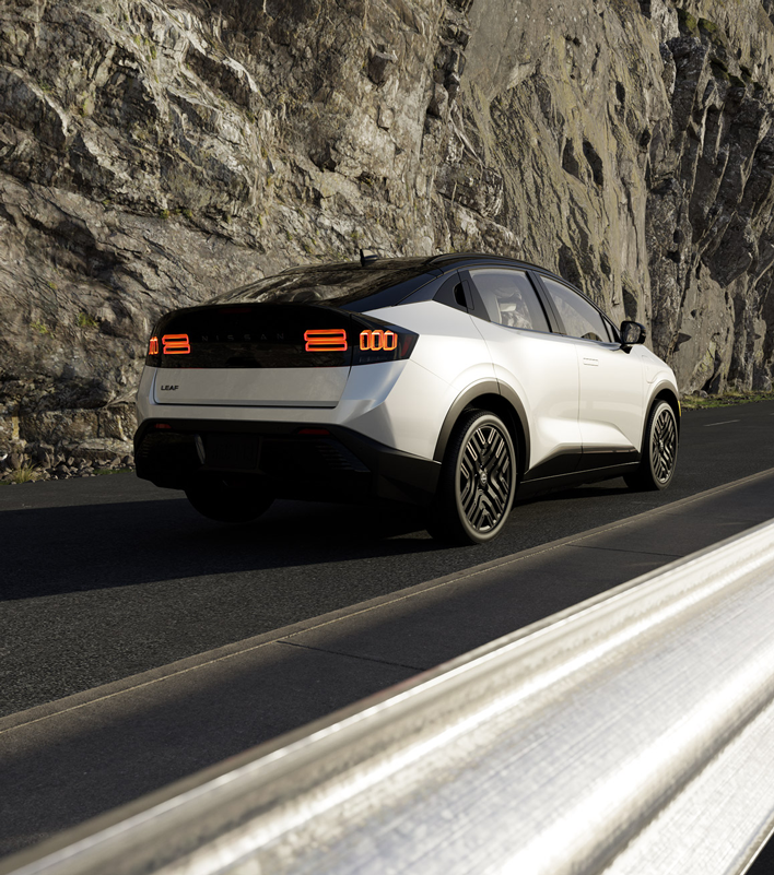 White car with black roof and wheels, driving on a road next to a rocky cliff.